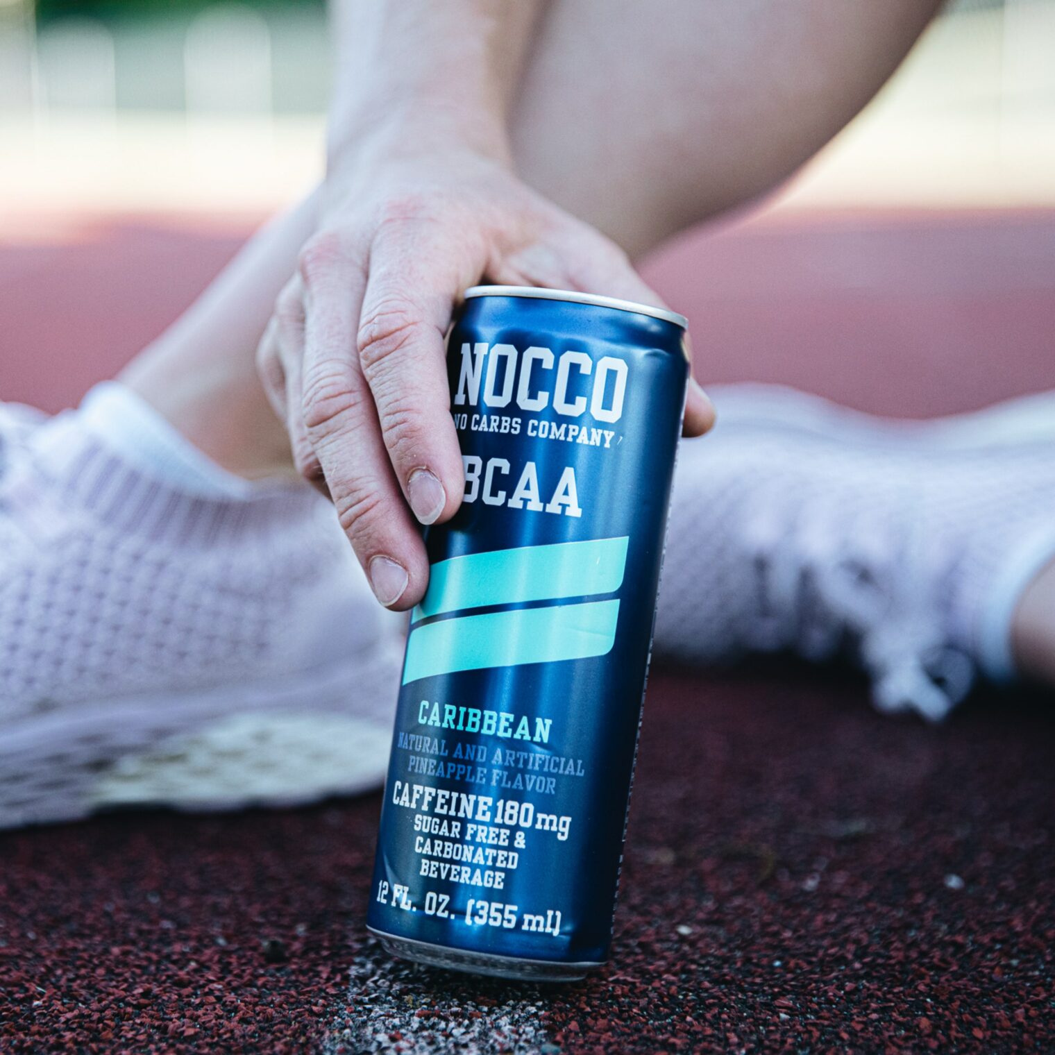 Hand holding a can of NOCCO BCAA drink on a running track.