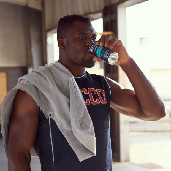 Man drinking from a can with a towel over his shoulder in a gym.