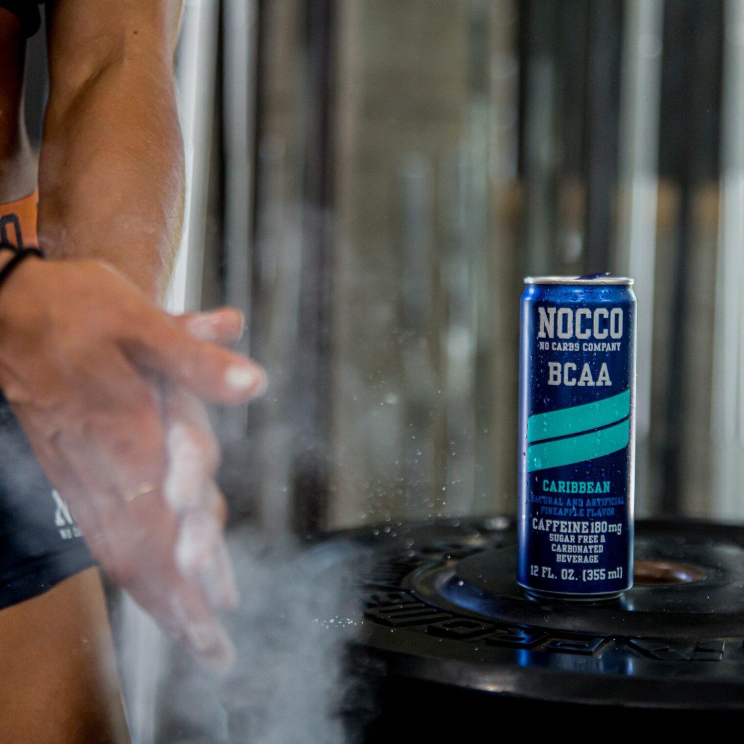 Gym setting with a person clapping hands covered in chalk dust near a NOCCO BCAA drink can.